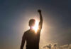 Silhouette of person with raised fist against sunset.