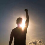 Silhouette of person with raised fist against sunset.