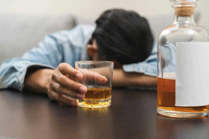 shutterstock_2474121053 Person asleep at table holding drink glass