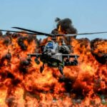 Attack helicopter flying in front of a massive explosion