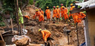 Rescue workers in orange uniforms search a landslide site with a dog