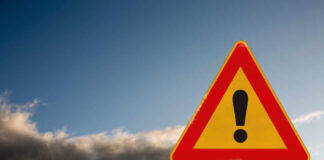 A triangular warning sign with an exclamation mark against a cloudy sky