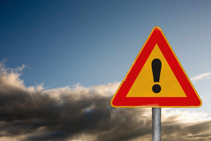 Attention,Road,Sign,On,A,Background,With,A,Dramatic,Sky A triangular warning sign with an exclamation mark against a cloudy sky