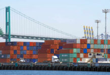 A view of stacked shipping containers at a port with a bridge in the background
