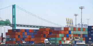 A view of stacked shipping containers at a port with a bridge in the background