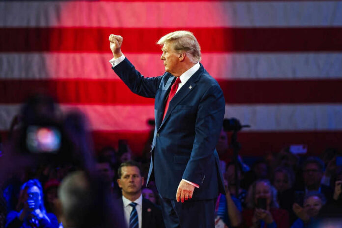 shutterstock24300674391jpg-1 Donald Trump raises a fist on stage before a large U.S. flag