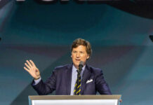 Tucker SLAMMED Over Hitler Spin Tucker Carlson speaking at a podium with a microphone