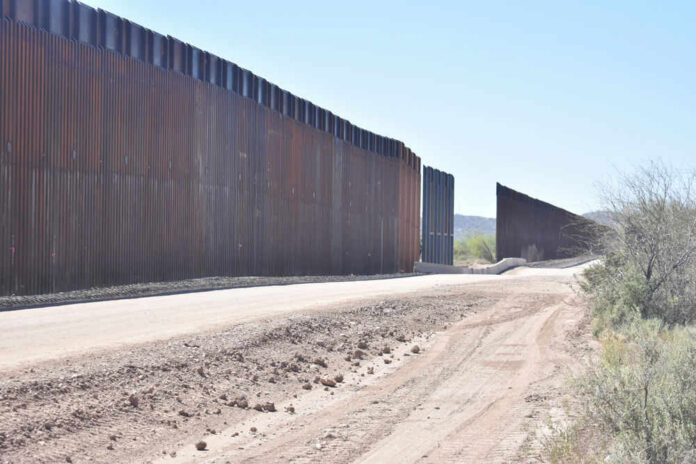shutterstock_1958049433 Dirt road beside tall metal border wall