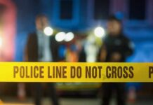 Police tape at a night scene with blurred officers in the background