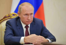 Putin Blinked: America Wins Vladimir Putin in a suit sits at a table.