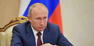 Vladimir Putin in a suit sits at a table.