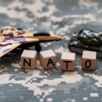 NATO’s Brutal Promise: Block, Blunt, Break Silhouetted operator with headset using laptop before American flag