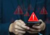 Hands holding a smartphone with red warning icons appearing on screen