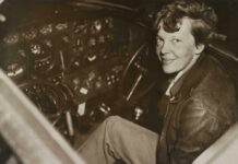 Earhart Clue Stuns Investigators Amelia Earhart seated in an airplane cockpit, looking toward the camera