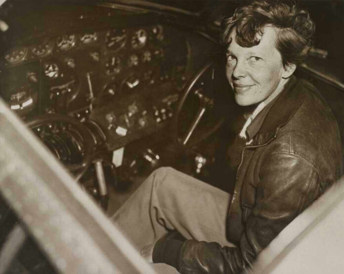 shutterstock_249572038-1 Amelia Earhart seated in an airplane cockpit, looking toward the camera