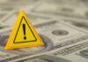 AI Sparks Power Bill Panic A yellow warning sign placed on a pile of dollar bills