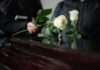 Two individuals placing white roses on a coffin during a funeral