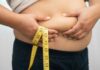 Person pinching belly fat while holding a yellow measuring tape
