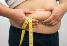 Person pinching belly fat while holding a yellow measuring tape