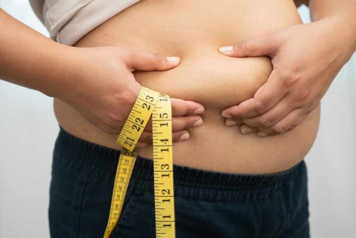 Person pinching belly fat while holding a yellow measuring tape
