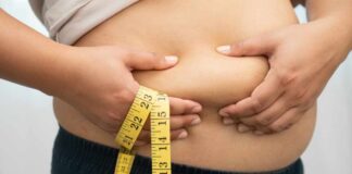 Person pinching belly fat while holding a yellow measuring tape