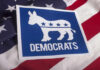 Feds Hit Democrat – Why Now? Democrats logo on American flag background.