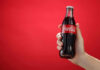 Hand holding a glass soda bottle against a red background
