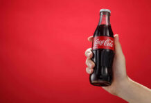 Hand holding a glass soda bottle against a red background