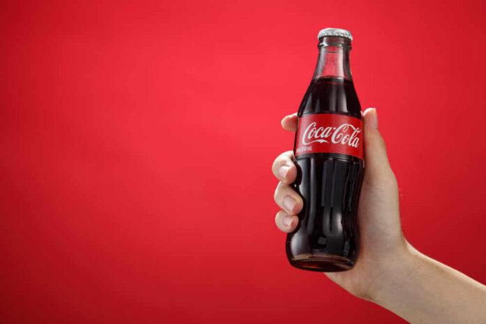 Hand holding a glass soda bottle against a red background