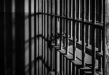 Killer Vanishes After Fence Breach Black and white photo of jail cell bars.